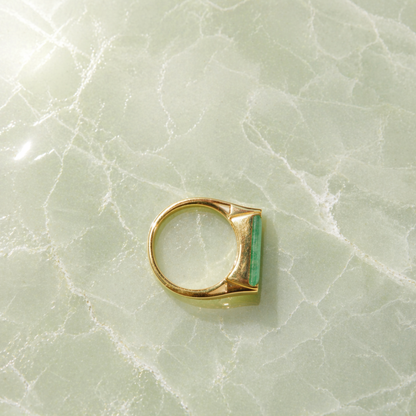 A handcrafted 18kt gold plated Calm Elegance Ring on a green marbled surface, showcasing the sleek rectangular green aventurine stone and the circular profile of the 925 sterling silver band.