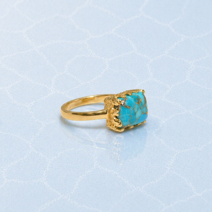 Side profile of the handcrafted Earthy Charm Ring featuring a thick rectangular copper turquoise stone set in 18kt gold plated 925 sterling silver on a light blue textured surface.