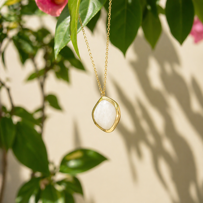 The Earthy Glow moonstone necklace hanging amongst green garden foliage in natural sunlight, capturing the soft shimmer and grounding character of the stone.
