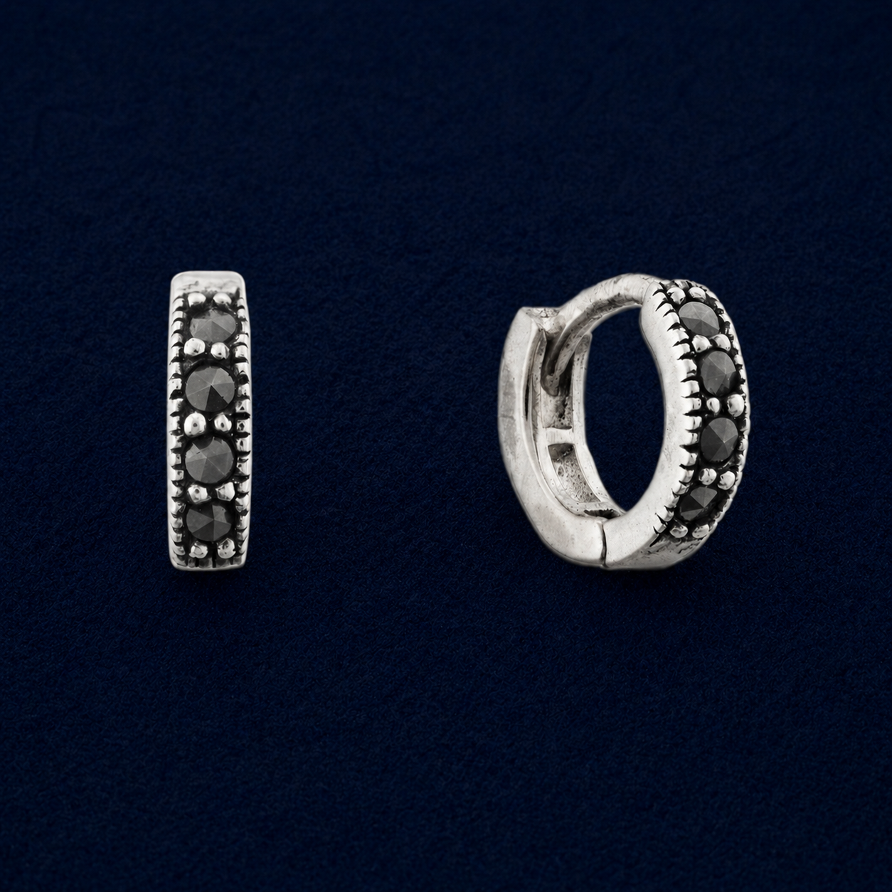 A pair of handcrafted Eclipse mini hoop earrings in 925 sterling silver, featuring an antiqued finish and a row of four round black cubic zirconia stones on a dark navy background.