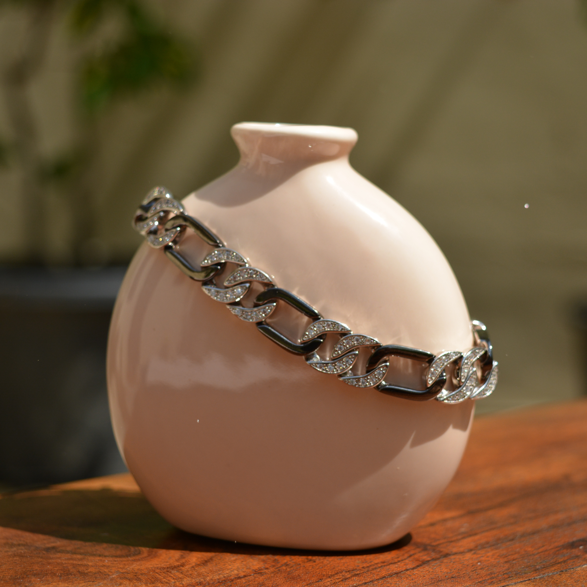 A handcrafted 925 sterling silver Effortless Edge link bracelet draped over a minimal beige ceramic vase, highlighting the contrast between the pavé CZ links and the polished black rhodium finish.