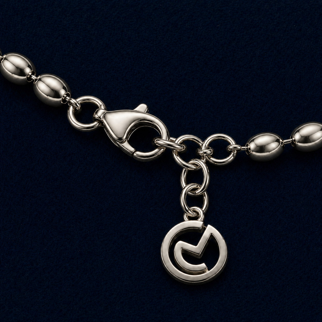 Macro close-up of a handcrafted 925 sterling silver bracelet featuring smooth oval links, a secure lobster clasp, and a polished circular logo charm against a dark navy background.