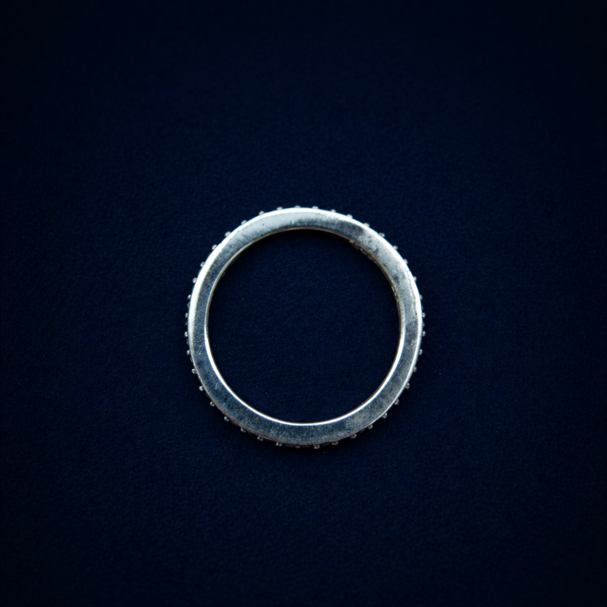 A top-down view of the handcrafted Everyday Sparkle Ring on a dark navy background, showcasing the clean circular silhouette and the delicate proportions of the 925 sterling silver band.