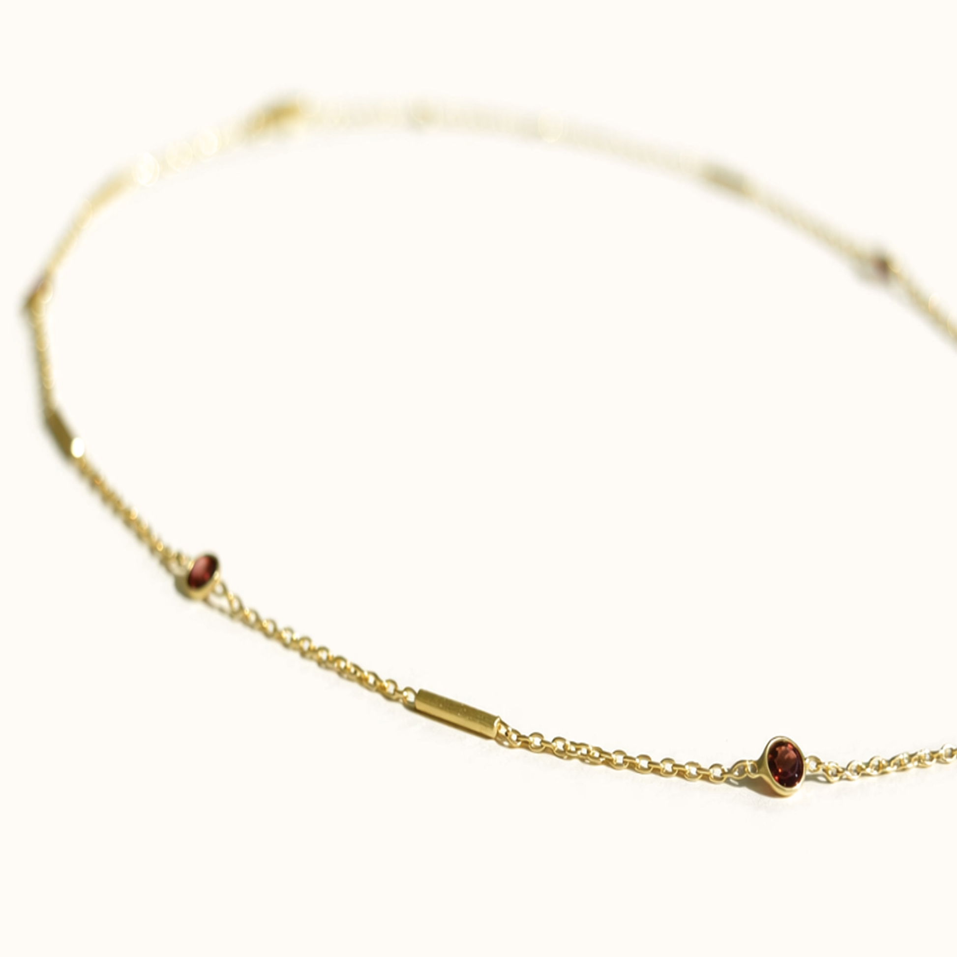 Perspective view of the Warm Glow Necklace on a white surface, highlighting the alternating pattern of deep red garnet stones and polished modern gold bars.