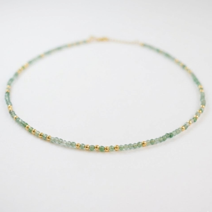 A perspective shot of the Nature’s Calm necklace on a white surface, highlighting the alternating pattern of small faceted green beryl, labradorite, and gold-plated sterling silver beads.