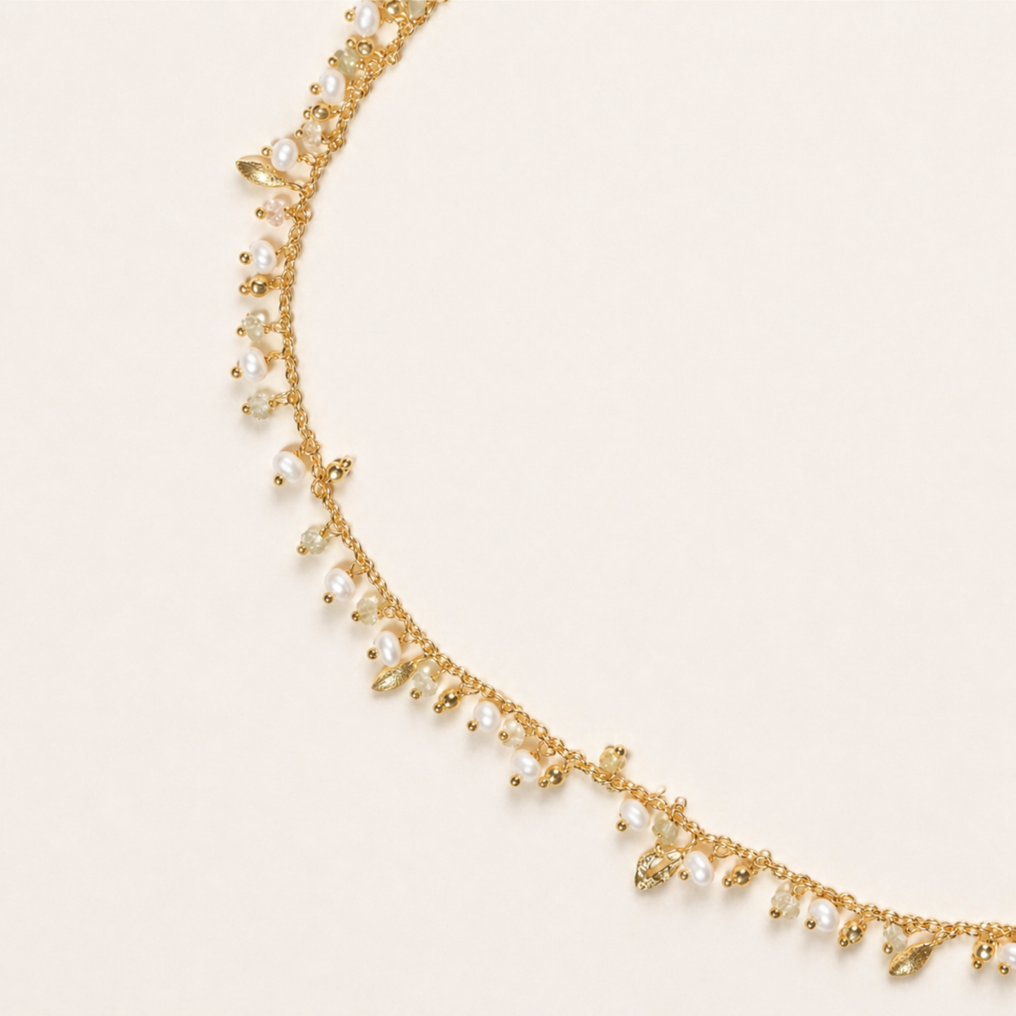 A detailed close-up of the Natural Grace necklace highlighting the rhythmic arrangement of small white pearls, earthy granite beads, and tiny gold leaf-shaped charms on a fine gold-plated chain.