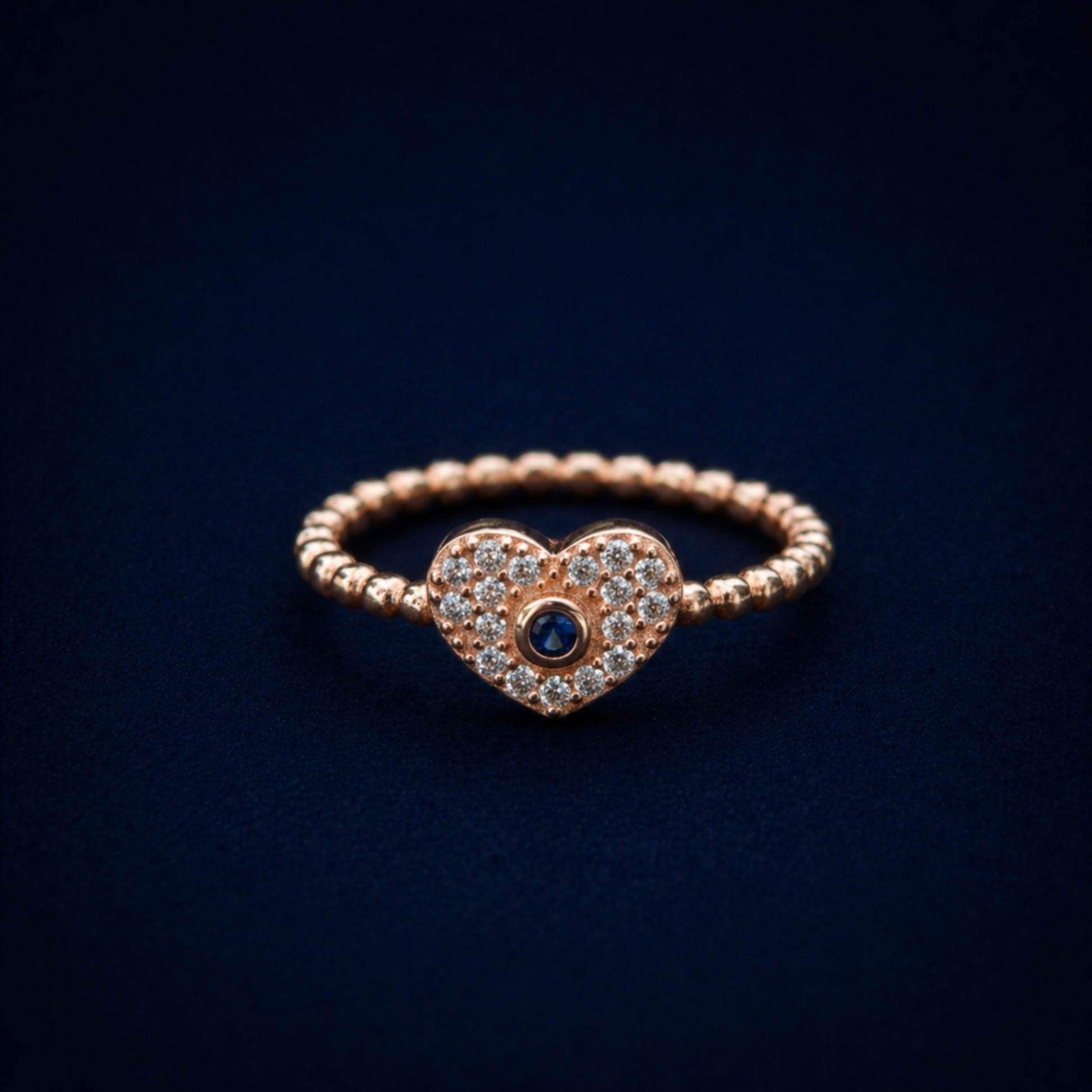Frontal view of the A Little Love Ring featuring a sparkling pavé-set heart with a central blue cubic zirconia stone on a polished rose gold plated silver band.