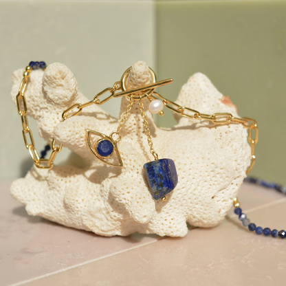 Close-up of the Meaningful Charm Necklace on a white coral prop, featuring the toggle clasp detail, natural lapis lazuli charms, and a delicate pearl accent.
