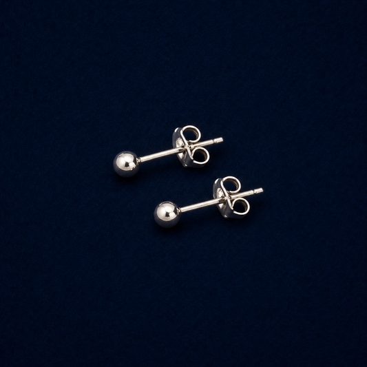 A pair of handcrafted Lunar Dot earrings in polished 925 sterling silver, featuring a minimal ball stud design with secure pushback closures on a dark navy background.