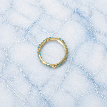 An overhead view of the Midnight Ball Ring, showcasing a continuous band of small blue-black jade beads set in 18kt gold plated 925 sterling silver on a blue marbled background.