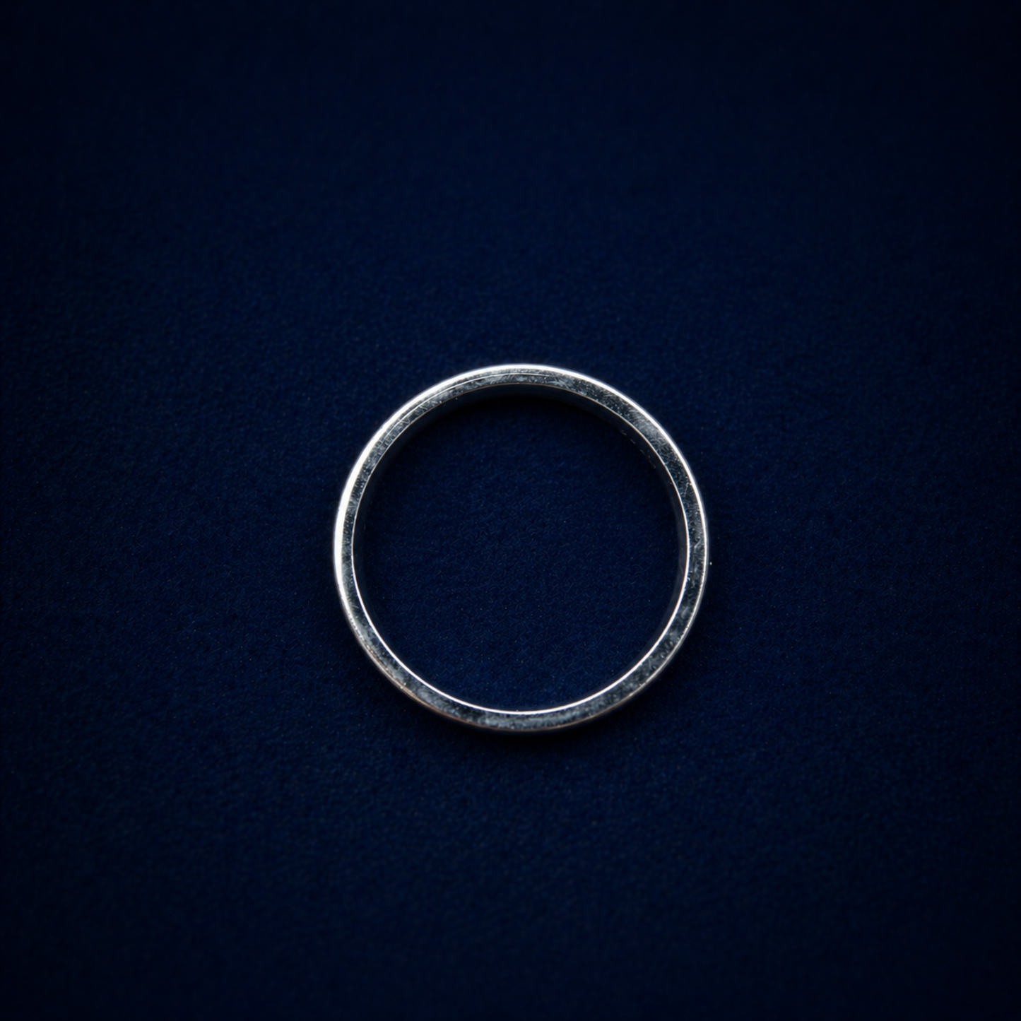 A top-down view of the handcrafted 925 sterling silver Midnight Edge Ring on a dark navy textured background, showcasing its perfect circular silhouette and minimal design.