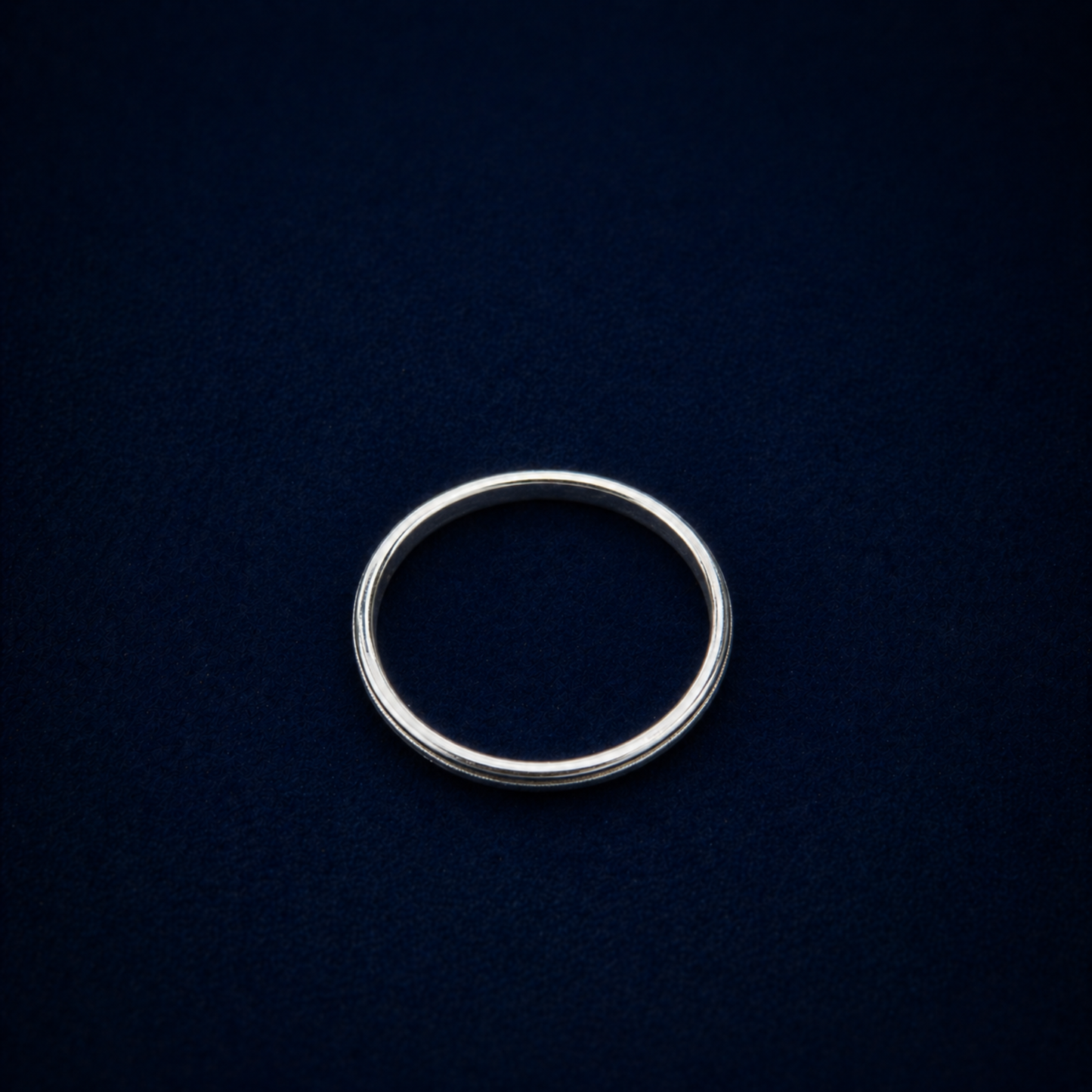Top-down view of the Glimmer Touch Ring on a dark navy background, showcasing the clean circular silhouette and delicate proportions of the silver band.
