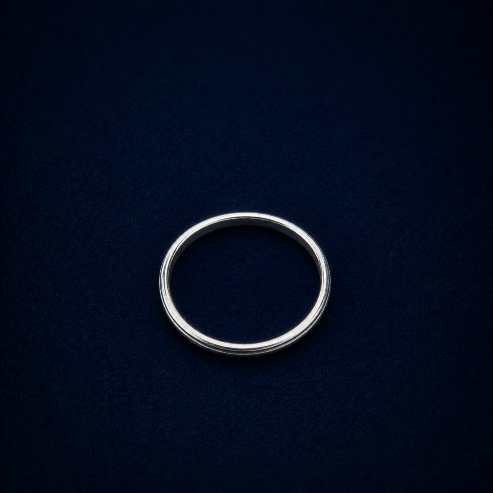 Top-down view of the Glimmer Touch Ring on a dark navy background, showcasing the clean circular silhouette and delicate proportions of the silver band.