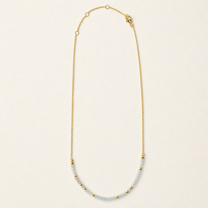 Full studio shot of the Earthy Ease necklace on a cream background, showcasing the alternating pattern of natural round granite stones and tiny gold-plated beads on a delicate chain.