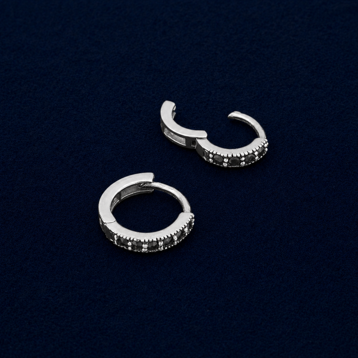 A detailed technical shot of the Eclipse mini hoops showcasing the secure click-to-close hinge mechanism and the  diameter profile, highlighting the textured silver border around the black pavé stones.