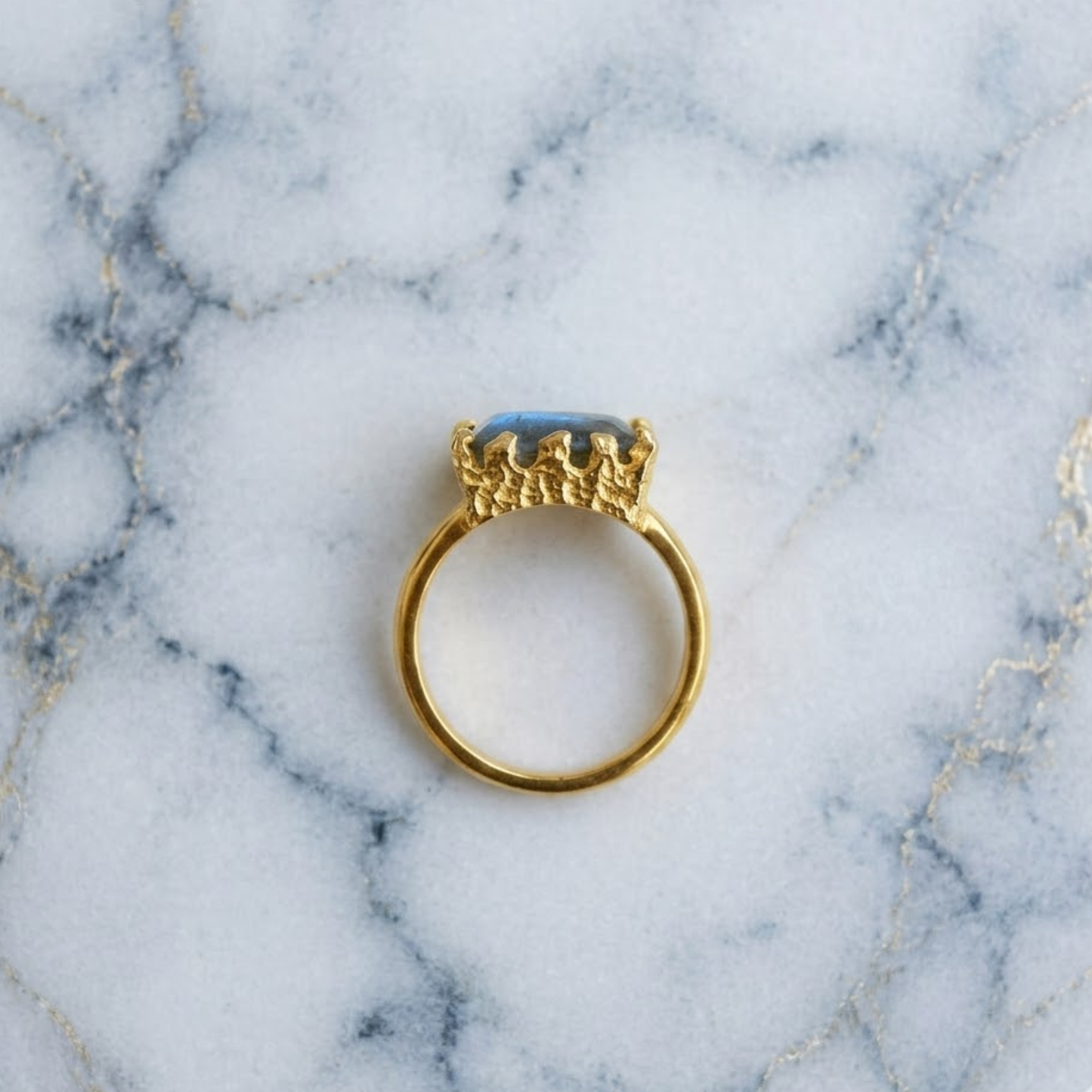 A handcrafted 18kt gold plated Mystic Glow Ring on a marble background, showing the unique textured setting and circular silhouette of the 925 sterling silver band
