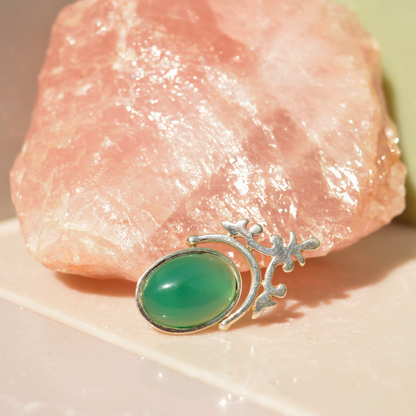 A handcrafted 925 sterling silver Natural Elegance pendant featuring an oval green onyx stone, displayed in front of a large raw rose quartz crystal for a luxurious lifestyle shot.