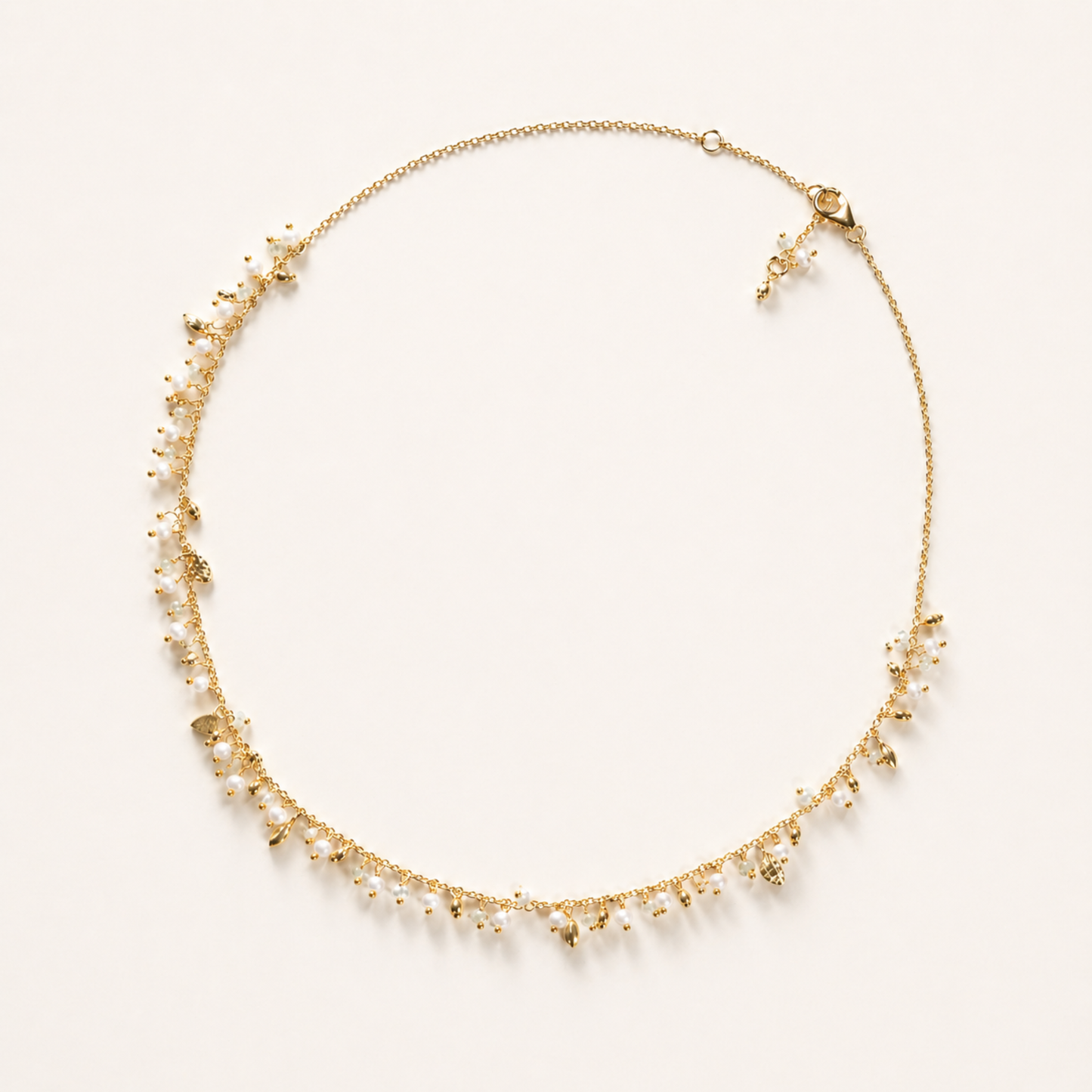 A full-length view of the handcrafted Natural Grace necklace in 18kt gold plated 925 sterling silver, featuring a delicate drop design of small hanging pearls and granite beads on a cream background.