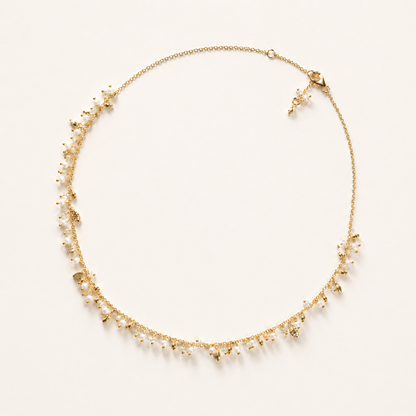 A full-length view of the handcrafted Natural Grace necklace in 18kt gold plated 925 sterling silver, featuring a delicate drop design of small hanging pearls and granite beads on a cream background.