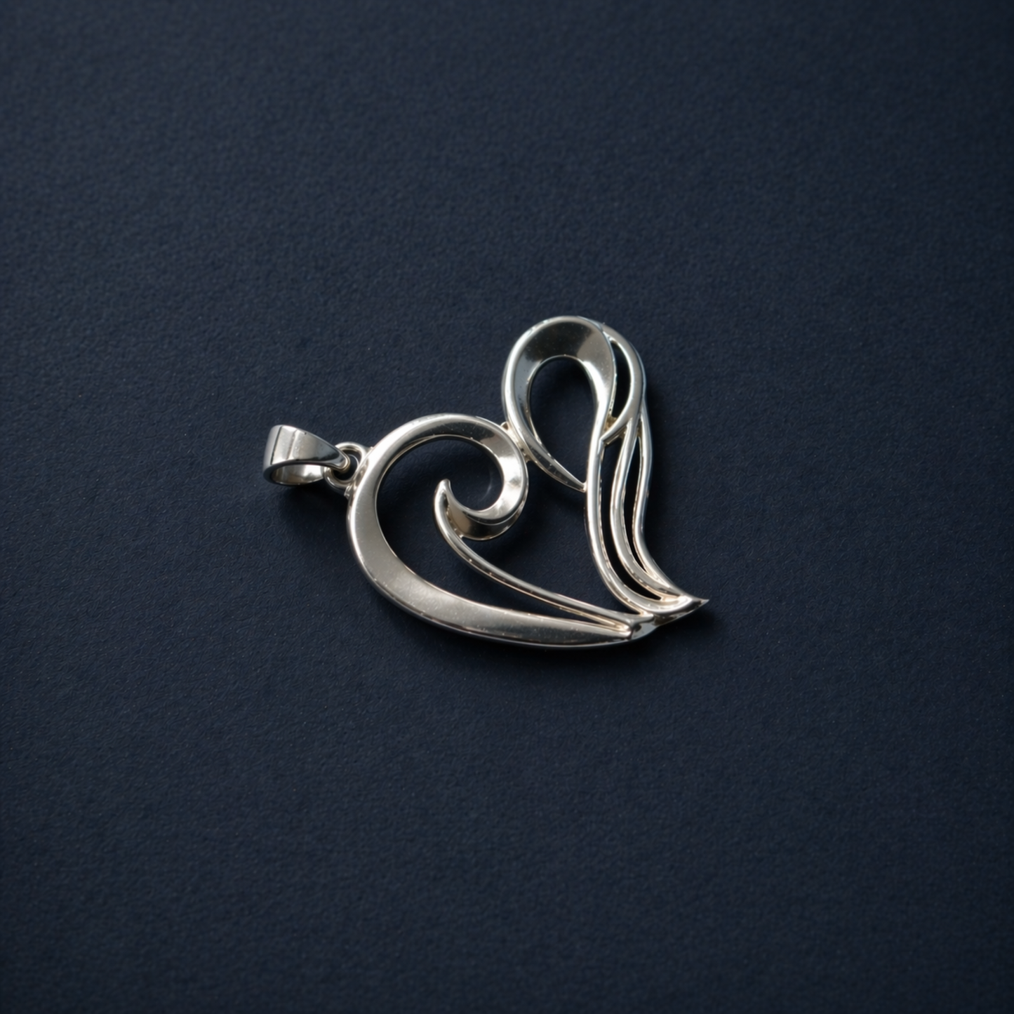 Flat lay view of the A Little Love Pendant on a dark textured background, highlighting the polished rhodium-plated finish and the elegant minimal wired heart silhouette.