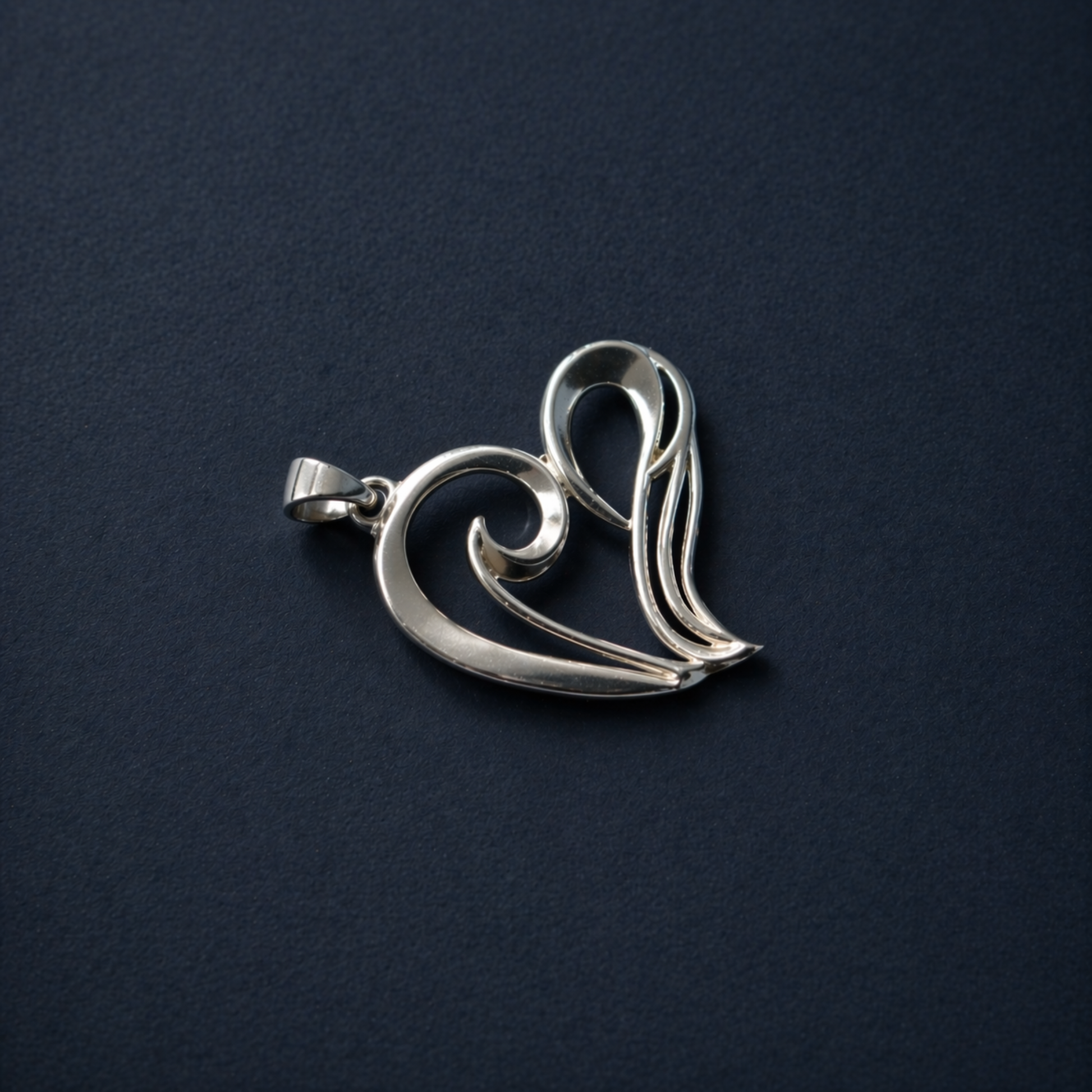 Flat lay view of the A Little Love Pendant on a dark textured background, highlighting the polished rhodium-plated finish and the elegant minimal wired heart silhouette.