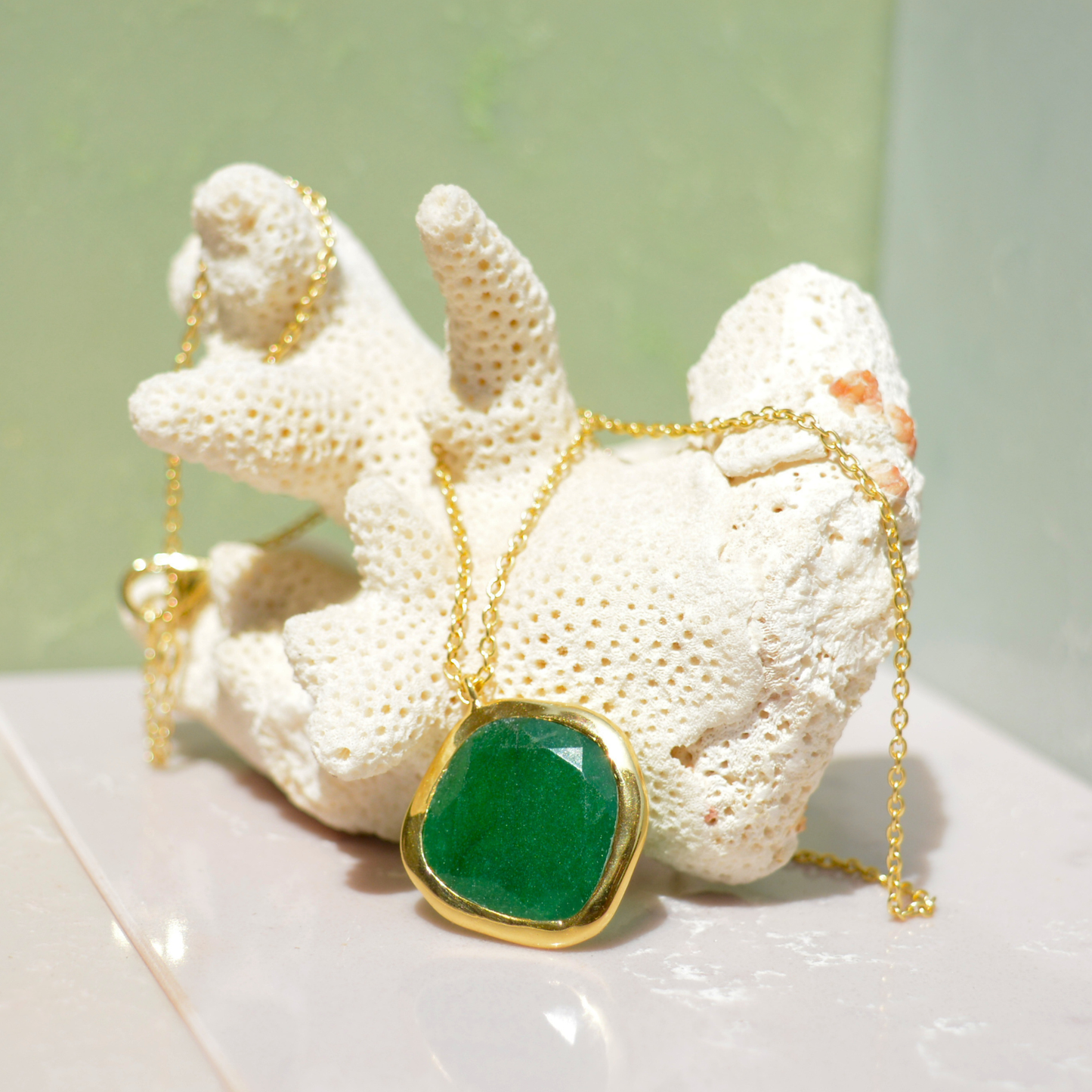Close-up of the Natural Pop necklace on a white coral prop, highlighting the rich vibrant green onyx and the slightly irregular handcrafted gold-plated frame.