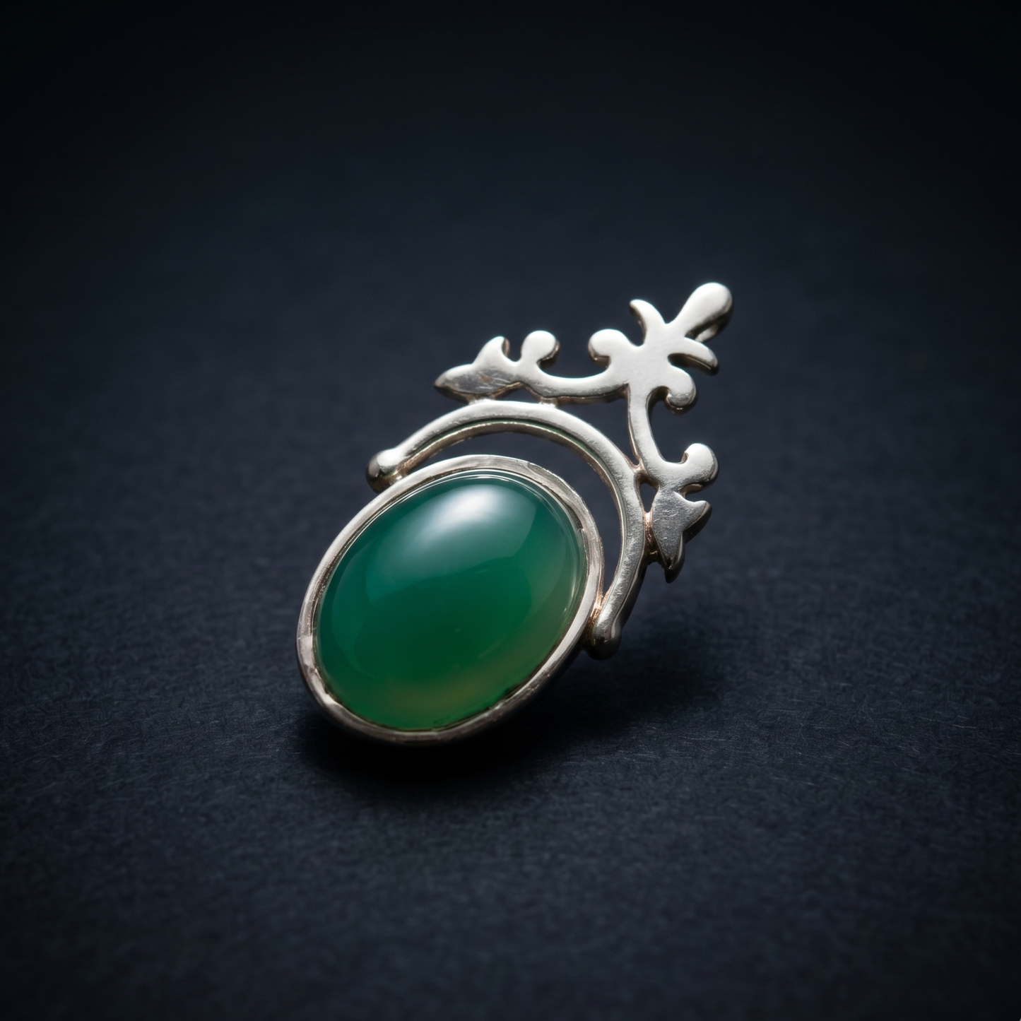 Close-up studio shot of the Natural Elegance pendant on a dark navy background, showcasing the polished oval green onyx and the elegant handcrafted silver silhouette.