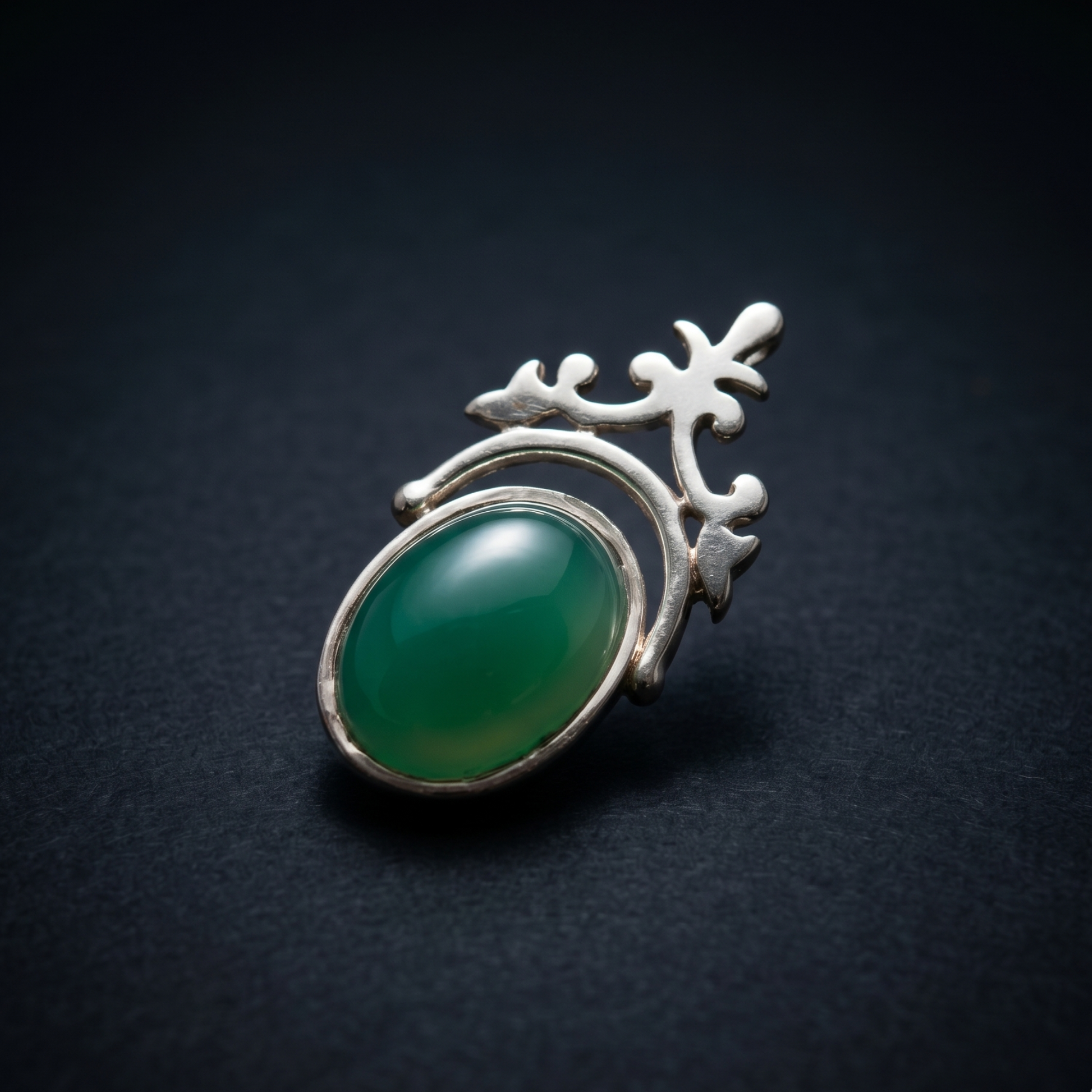 Close-up studio shot of the Natural Elegance pendant on a dark navy background, showcasing the polished oval green onyx and the elegant handcrafted silver silhouette.
