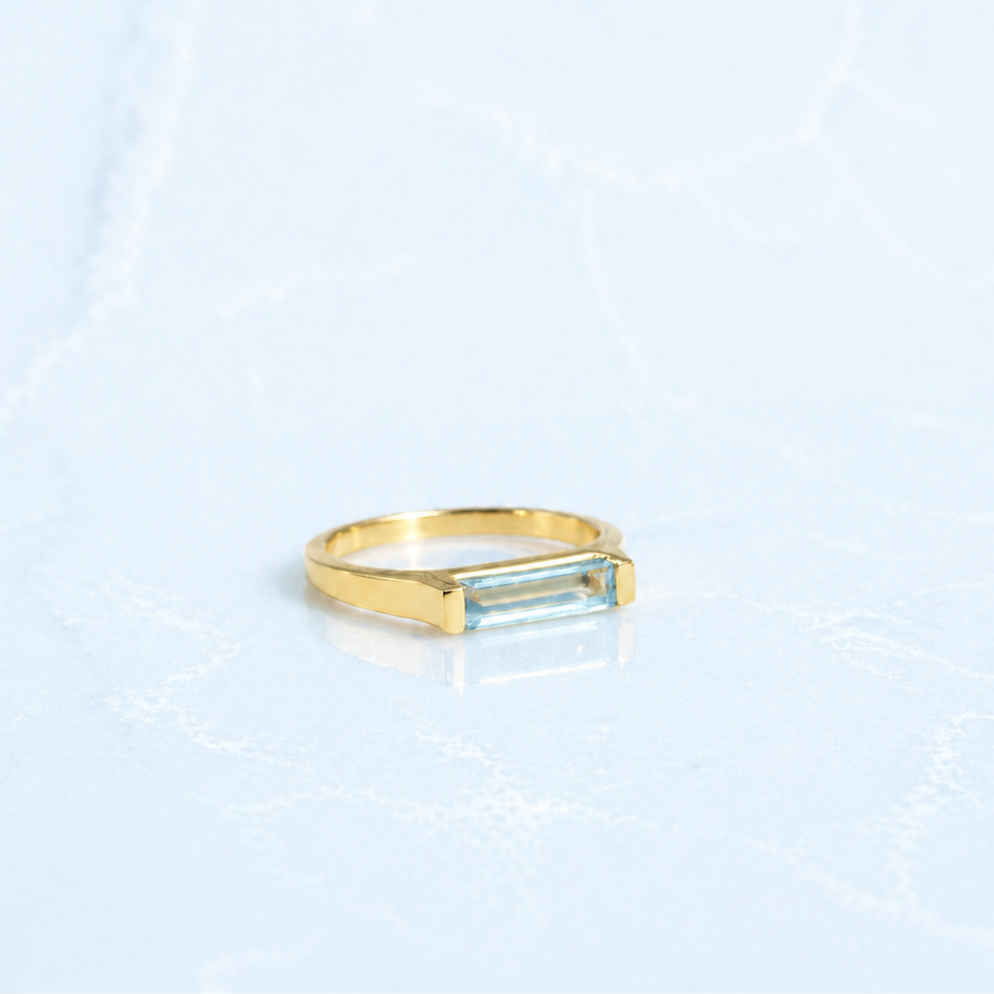 Side view of the Sky Glow Ring showing the modern structured setting of the rectangle-cut blue topaz and the slim, comfortable gold plated profile.