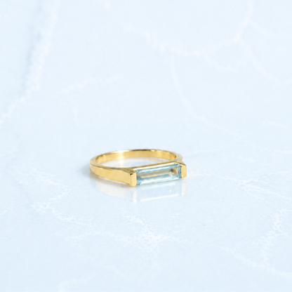 Side view of the Sky Glow Ring showing the modern structured setting of the rectangle-cut blue topaz and the slim, comfortable gold plated profile.