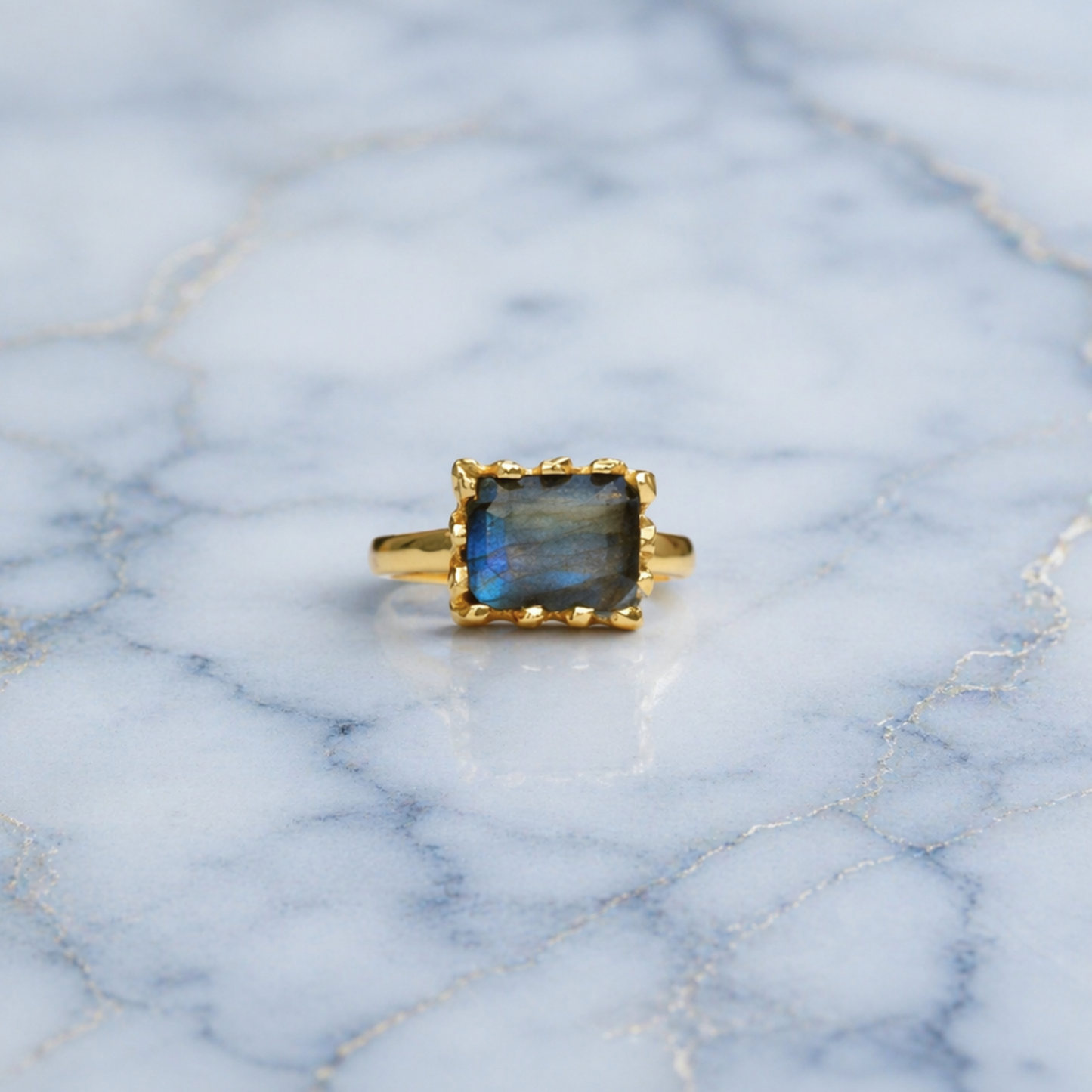 Frontal view of the Mystic Glow Ring featuring a thick rectangular labradorite stone with natural blue flashes, set in a polished gold plated minimal frame on marble.