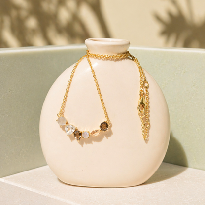 A handcrafted 18kt gold plated Soft Harmony necklace with labradorite, morganite, and smoky quartz stones, draped over a minimal beige ceramic vase.