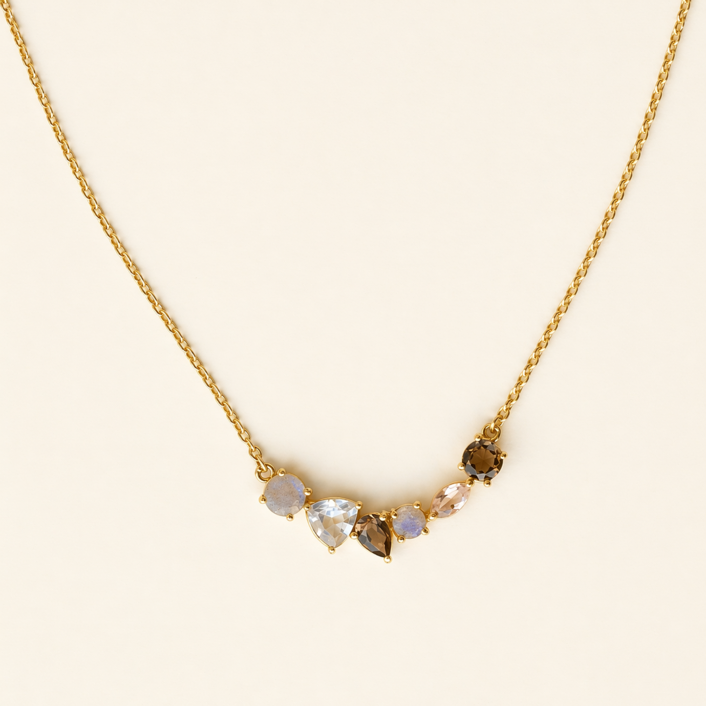 Frontal view of the Soft Harmony necklace on a cream background, showcasing the balanced arrangement of multi-shaped clear quartz and smoky quartz stones on a delicate gold chain.