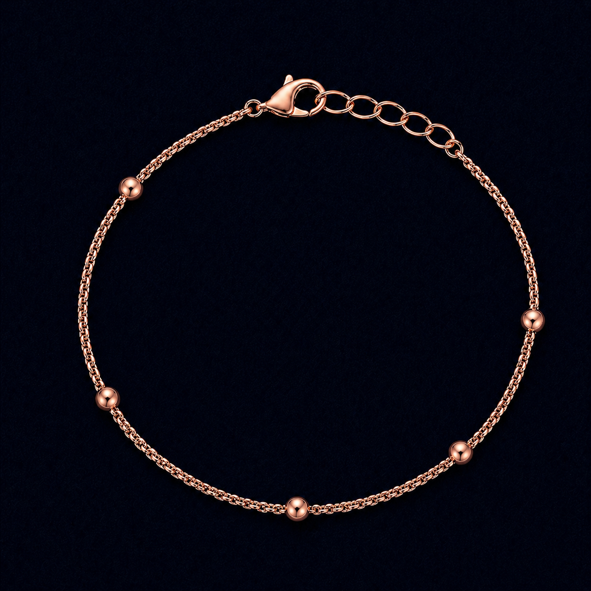 A full-length studio shot of the handcrafted Subtle Circles bracelet in a rose gold finish, featuring five polished spherical beads spaced along a delicate linked chain on a dark navy background.