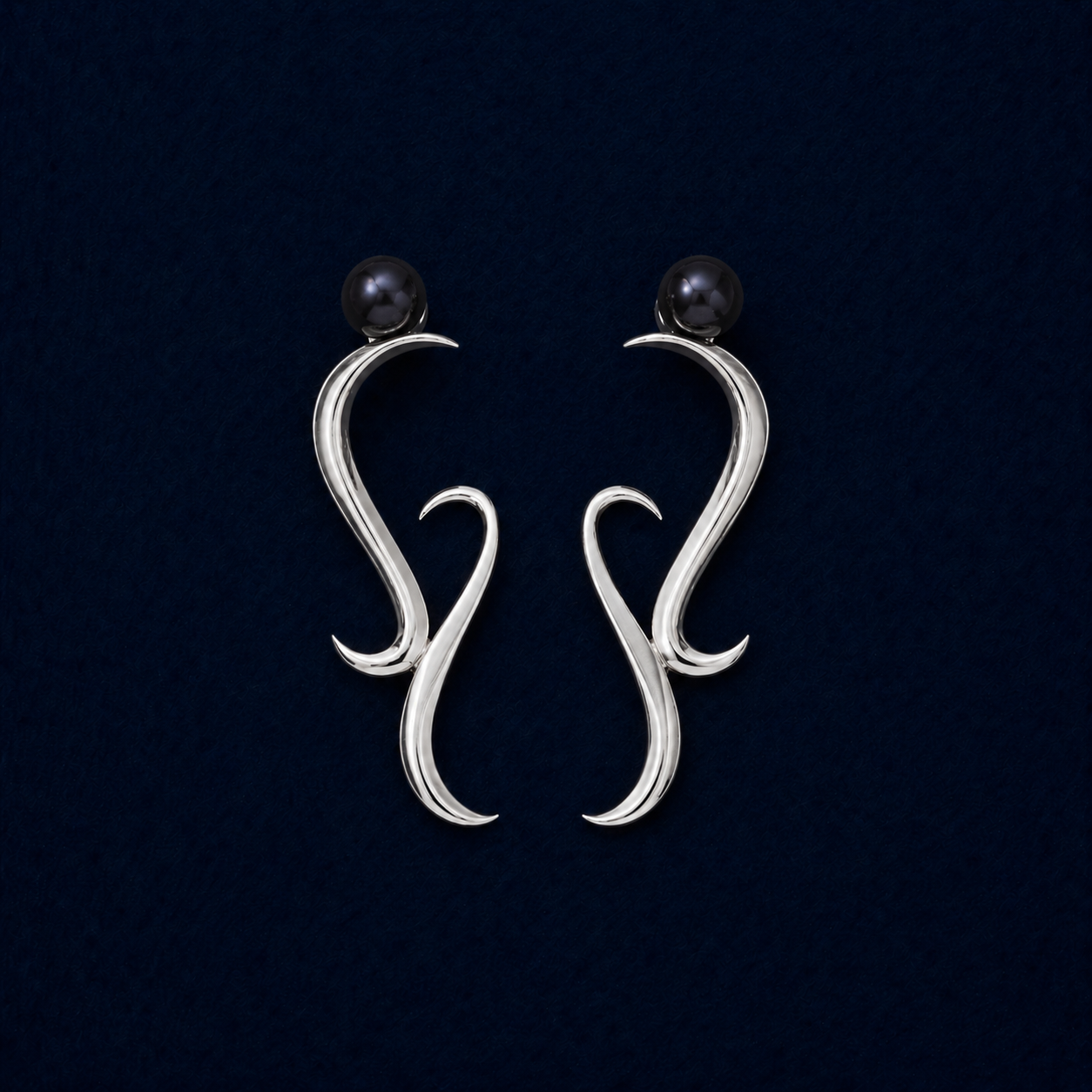 A symmetric studio shot of the handcrafted Symphony earrings in rhodium-plated brass, featuring a modern wavy architectural design topped with sophisticated dark blue water pearls on a navy background.