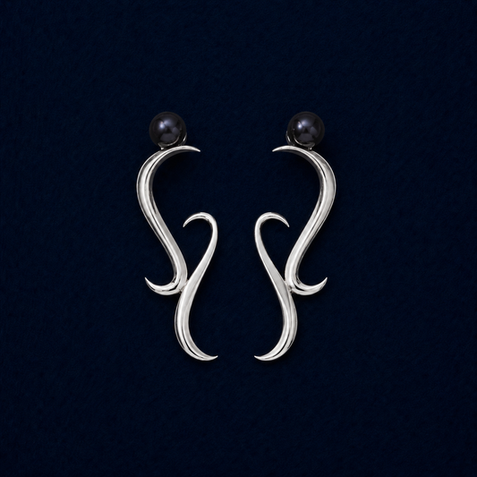 A symmetric studio shot of the handcrafted Symphony earrings in rhodium-plated brass, featuring a modern wavy architectural design topped with sophisticated dark blue water pearls on a navy background.