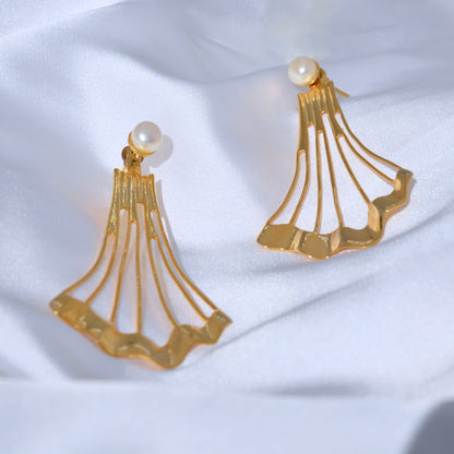 Pair of gold statement earrings featuring a single white pearl post and a wide, fanned-out geometric drop design on white silk.
