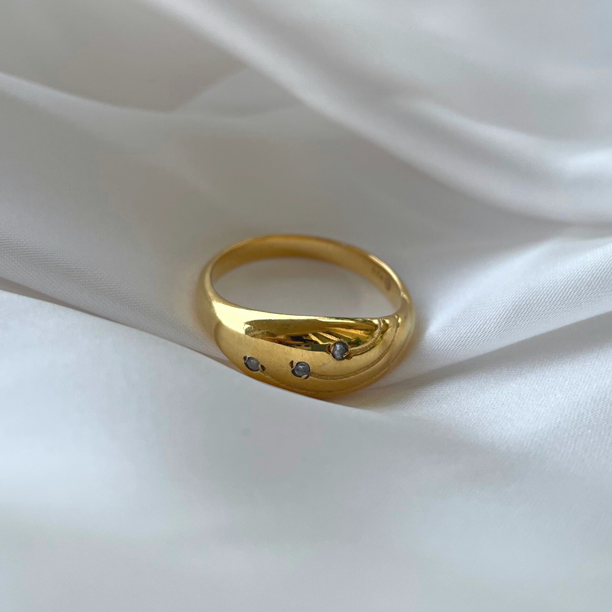 A gold dome ring featuring three sparkling stones, displayed elegantly on white silk.