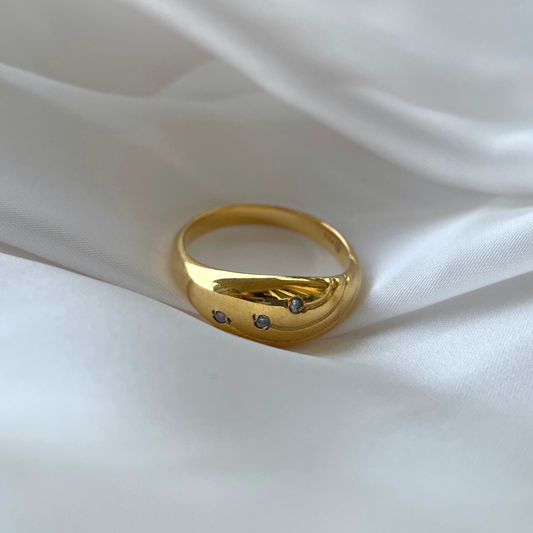 A gold dome ring featuring three sparkling stones, displayed elegantly on white silk.
