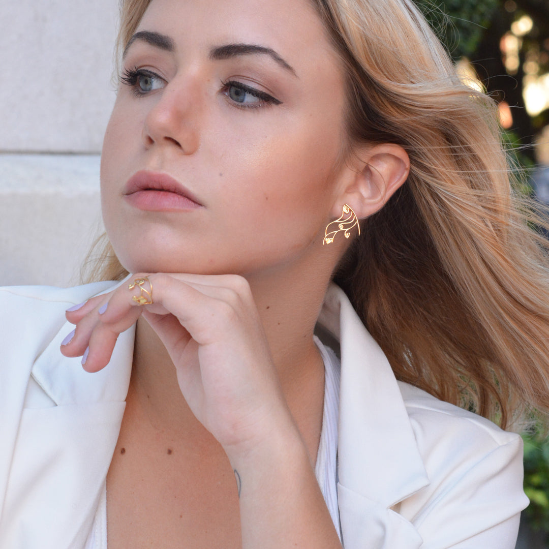 Close-up of a blonde model wearing a gold filigree vine earring in her lobe with a matching delicate gold ring.