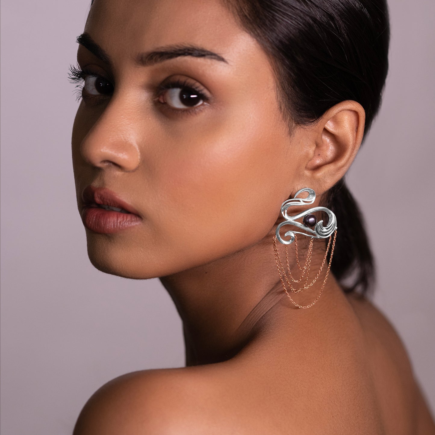 Close-up of a model wearing long, majestic silver earrings with a mix of rose gold and platinum finishes, inspired by oceanic aesthetics.