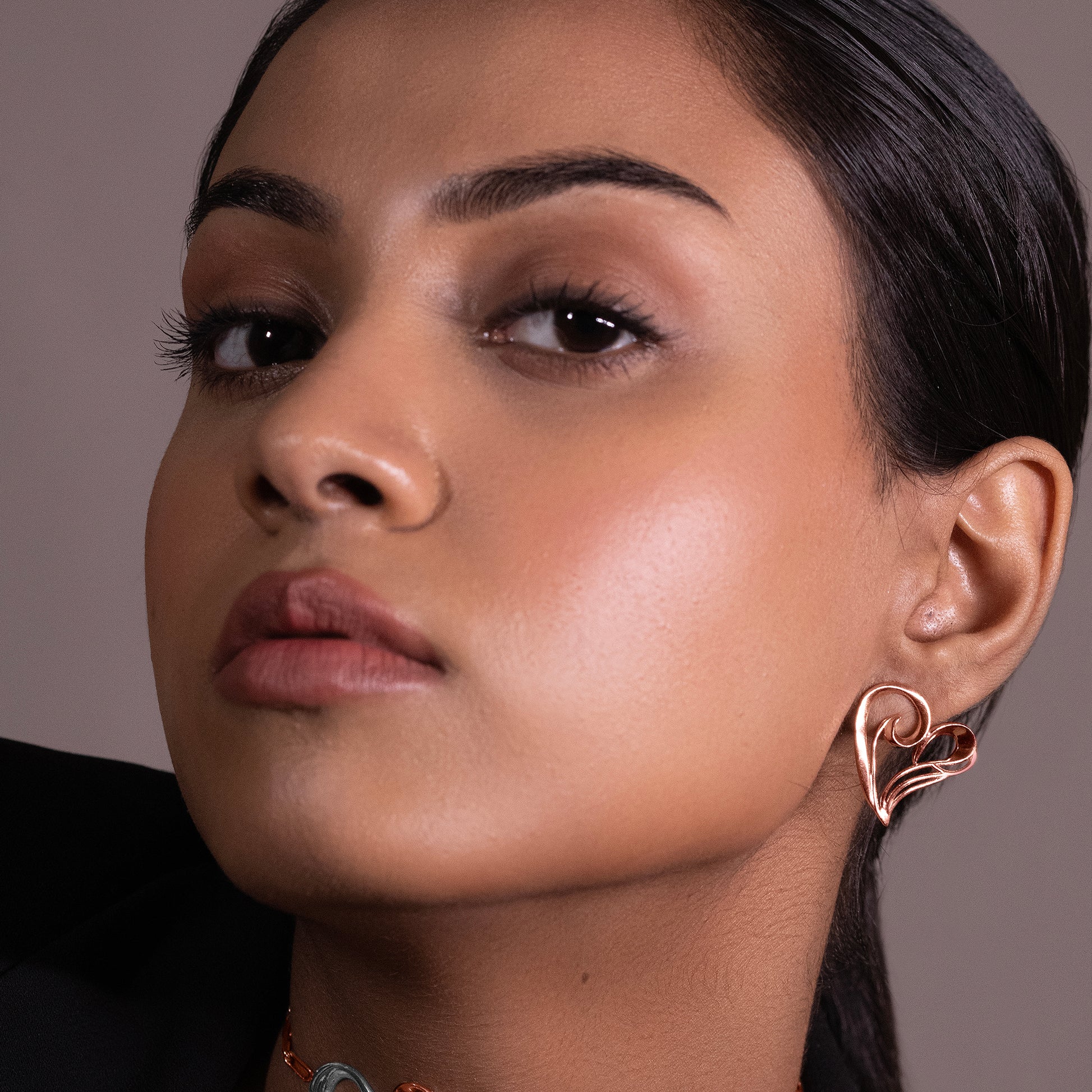 A portrait of a model wearing dainty, heart-shaped rose gold earrings that offer a sophisticated, warm glow against the skin.