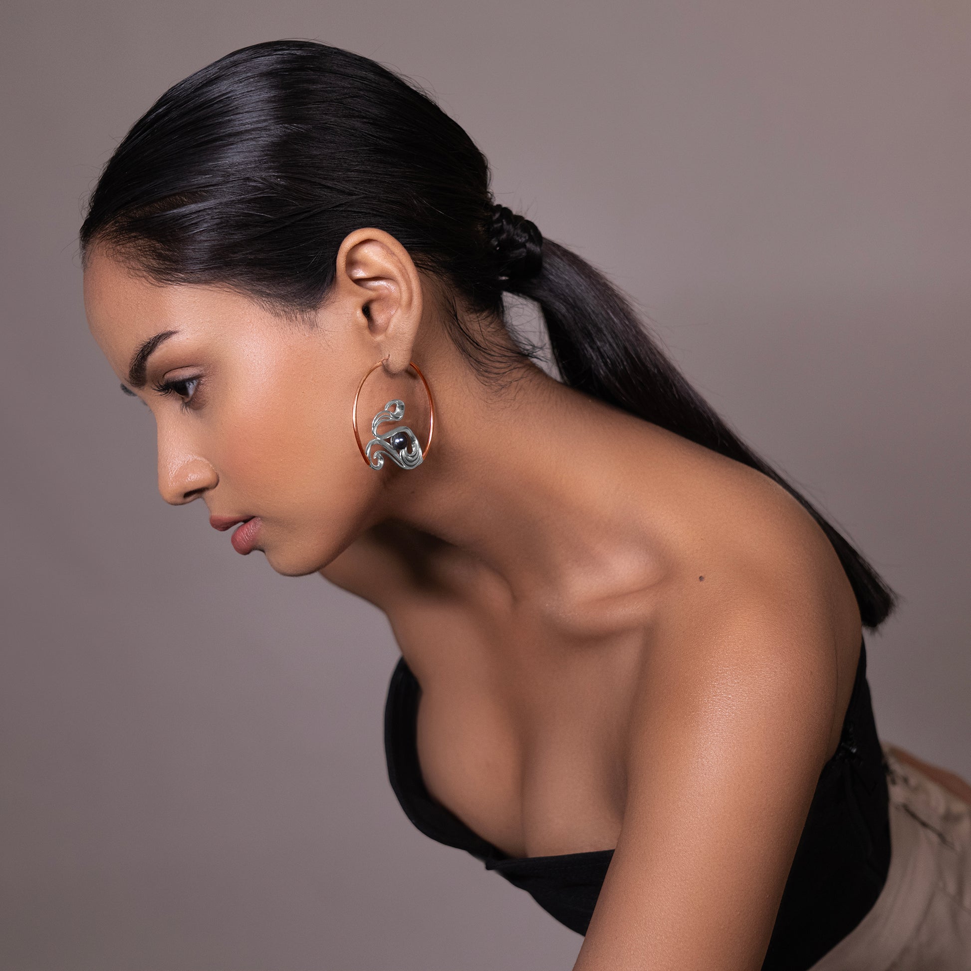 A model wearing sculptural silver-toned open hoop earrings with a thick, textured wave pattern against a clean studio background.