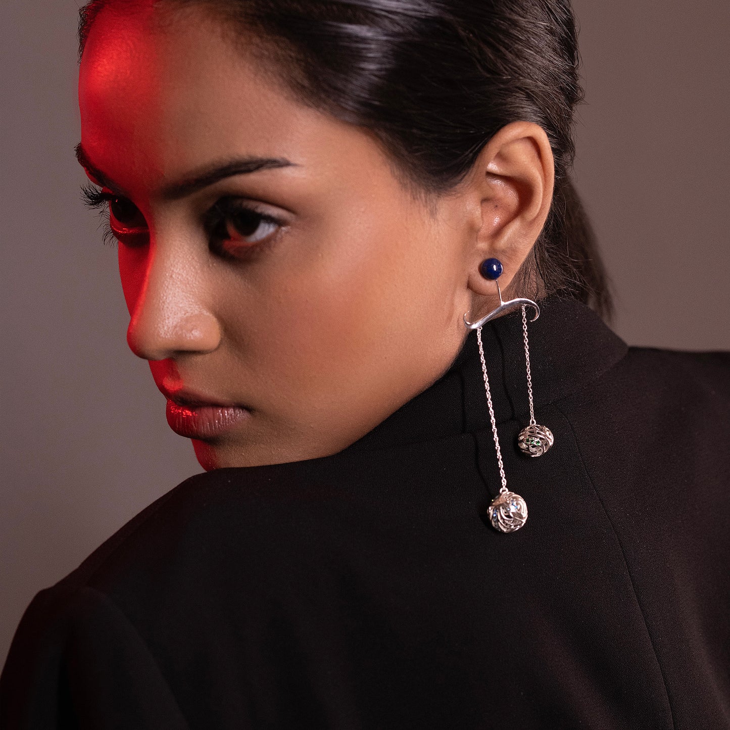 Close-up of a person wearing silver wave-patterned earrings with blue gemstones, highlighting a sophisticated and artistic jewelry style.