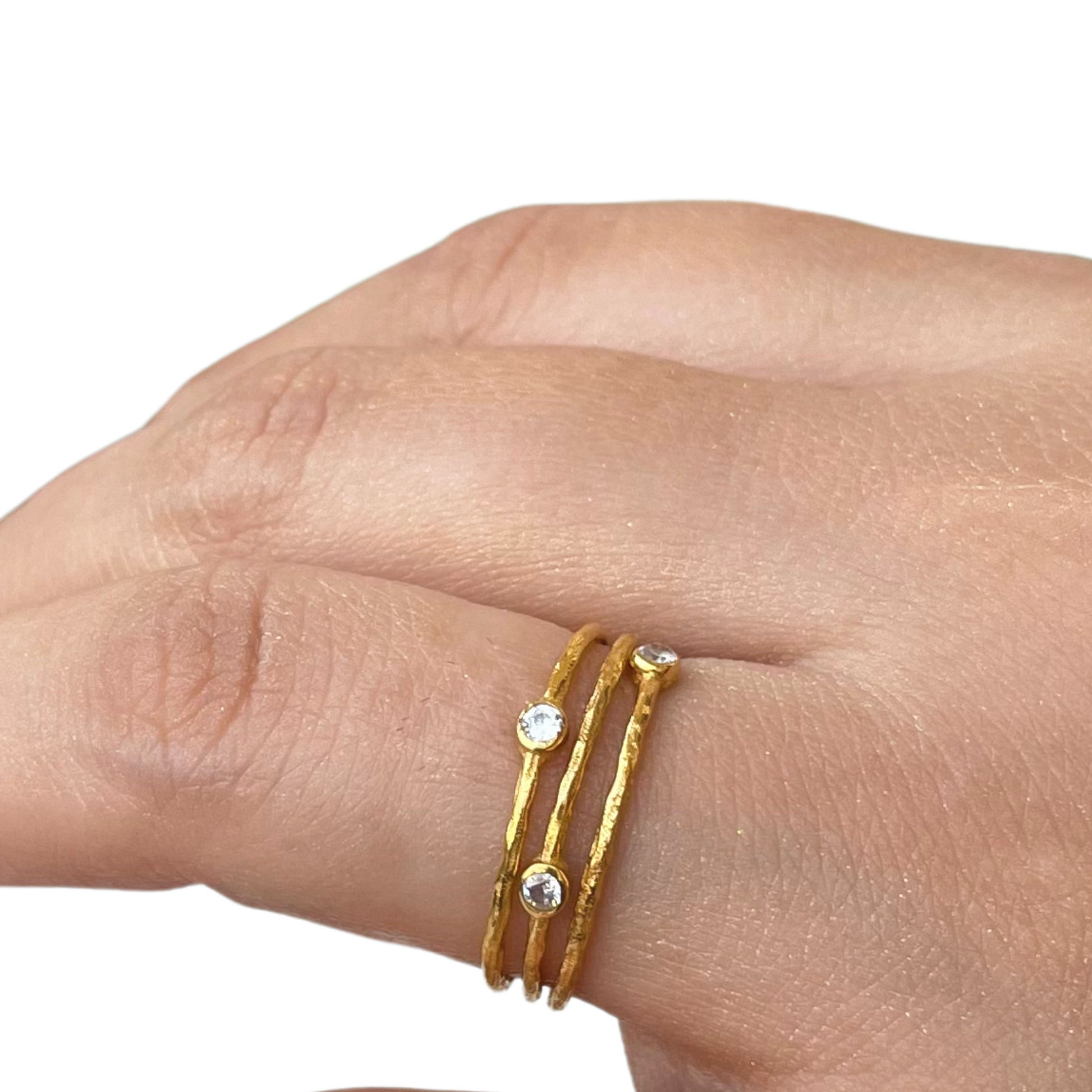 Close-up of a hand wearing three dainty gold-textured rings stacked together, each featuring a single shimmering bezel-set stone.