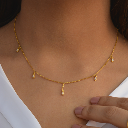 A person wearing a delicate yellow gold chain with subtle stations that gracefully drape across the collarbone, showcasing an understated and modern look.