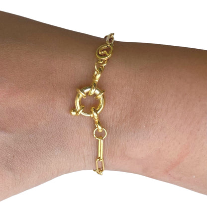 Close-up of a person's wrist wearing a dainty gold link bracelet with a high-shine finish and a circular statement fastener.