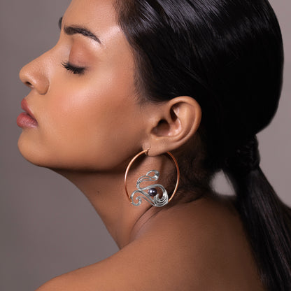 Close-up of a model wearing a large silver statement hoop earring with a unique wave-inspired geometric silhouette and polished finish.