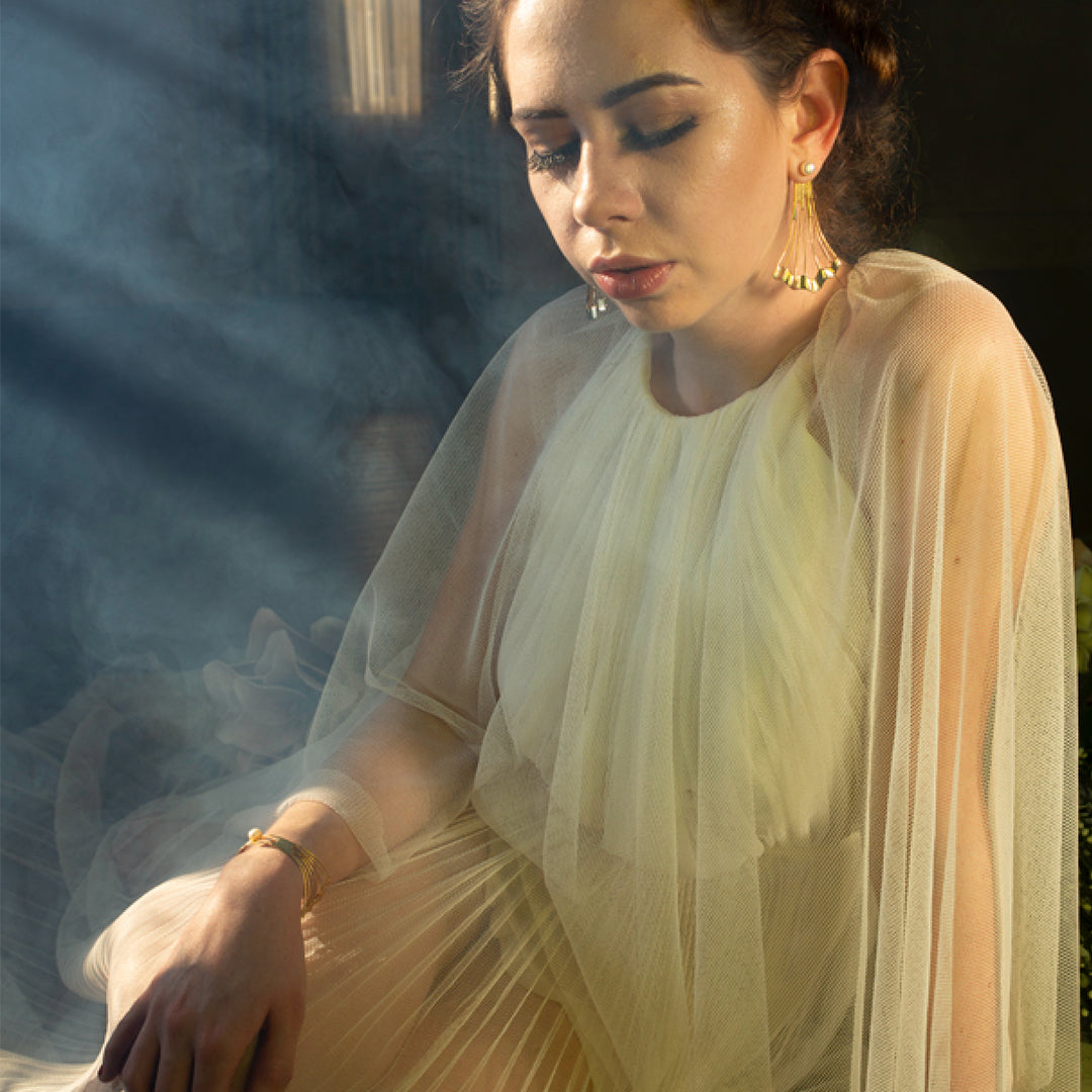 Model wearing gold architectural drop earrings with pearl accents and a matching multi-strand gold bracelet.