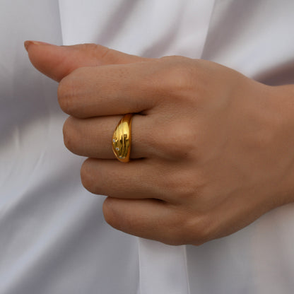 A hand wearing a polished gold dome ring with three delicate, sparkling stones, set against a white fabric background.